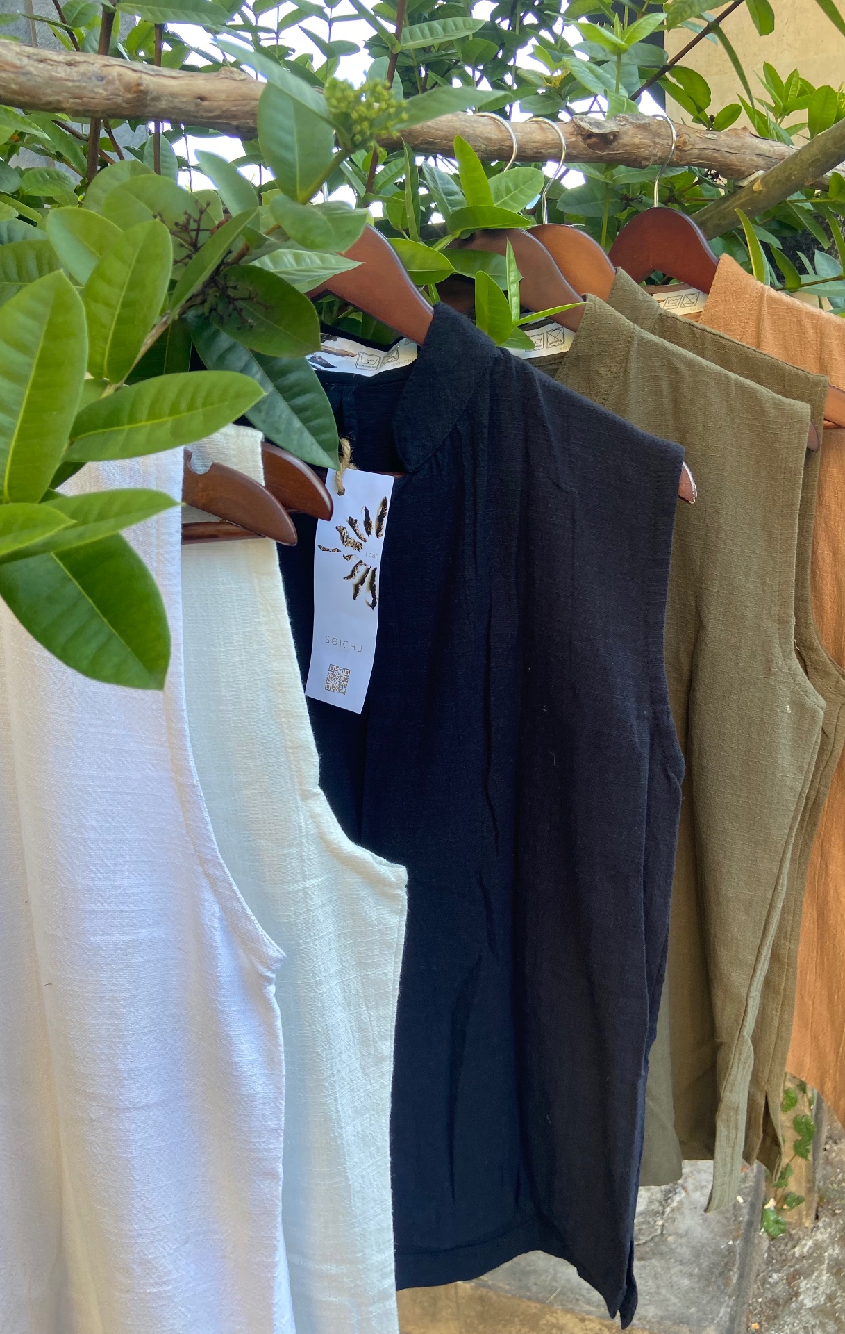 SOICHU vests in ivory, black, olive and terracotta hanging on a wooden branch
