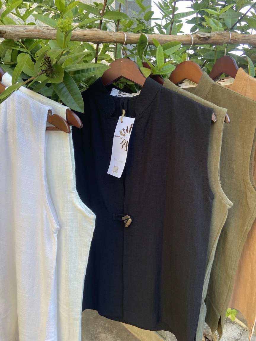 A black SOICHU vest with its handwritten SOICHU hang tag, next to ivory and olive vests